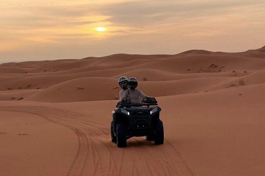 A person riding an ATV on a sand dune during sunset. 2