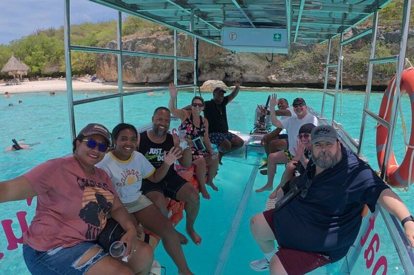 Een groep mensen op een boot, met helder turquoise water en een strand in de verte. 2