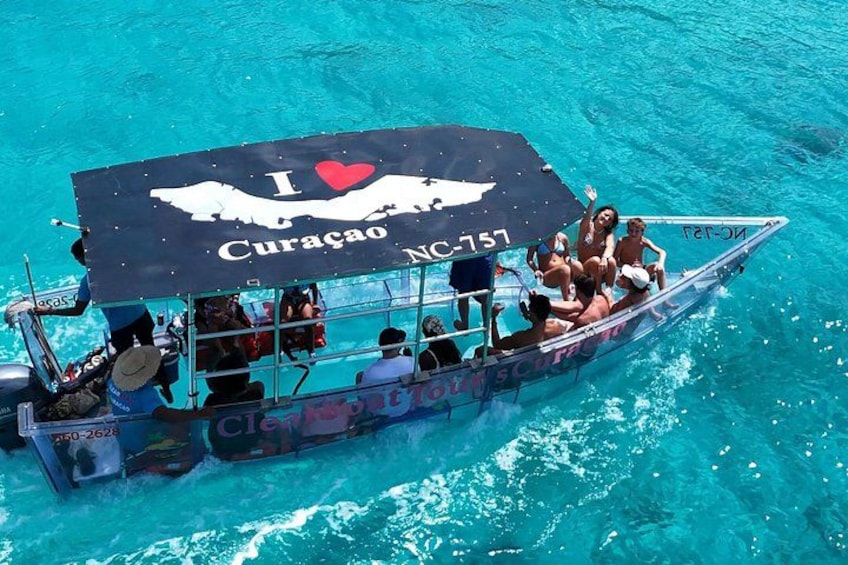 A boat with people on it, a clear blue sea, and a sign that says 'I love Curacao.' 1