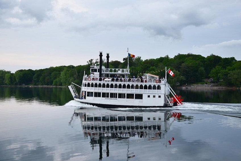 A white riverboat with multiple decks and flags, moving on calm water with a forested shoreline in the background. 4