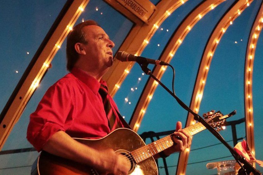 A person playing an acoustic guitar on a stage with string lights in the background. 5