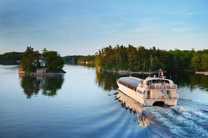 A riverboat moving on calm water, surrounded by dense forest and a small island with a house. 1