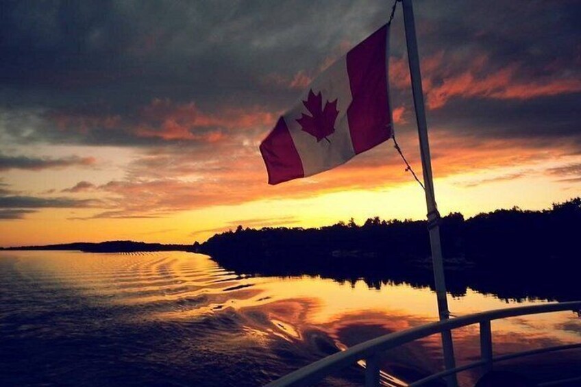 Una bandera canadiense ondeando en un asta, un cuerpo de agua reflejando el cielo y una puesta de sol. 2