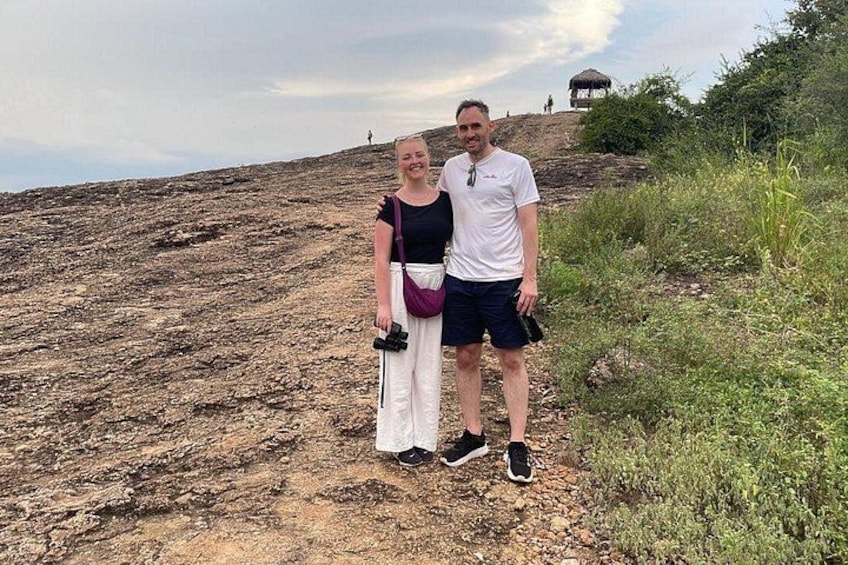 Two people standing on a rocky hillside with sparse vegetation. 3