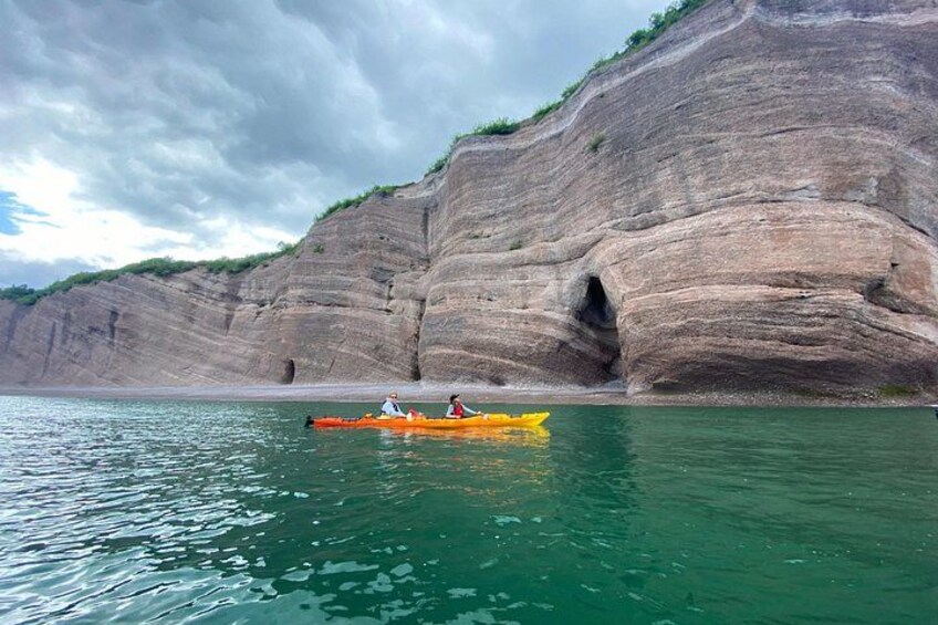 A kayaker in a yellow kayak on calm water near a large rock formation. 5