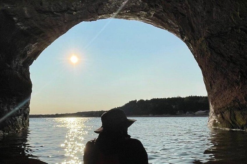 A person in a cave with a view of the sun over water. 4