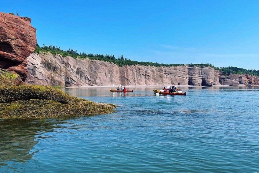A calm river with kayaks, rocky cliffs, and sparse vegetation. 3
