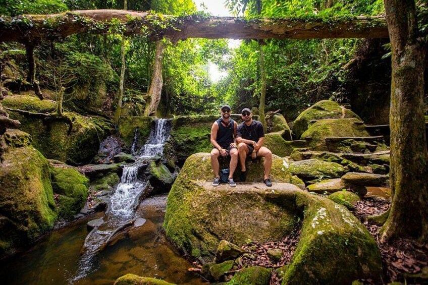 A waterfall, moss-covered rocks, and two people sitting on a rock. 4