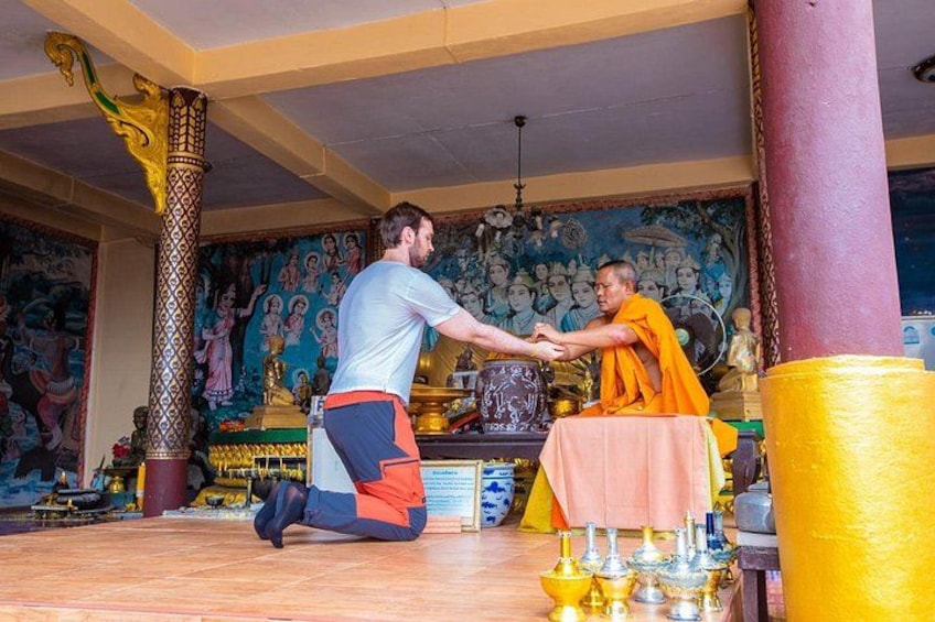 A person in a white shirt and orange robe kneeling and shaking hands with another person in a white shirt. 2