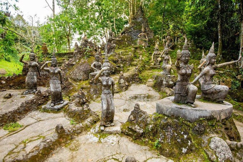 Stone statues of figures in various poses, set in a forested area with moss-covered rocks. 5