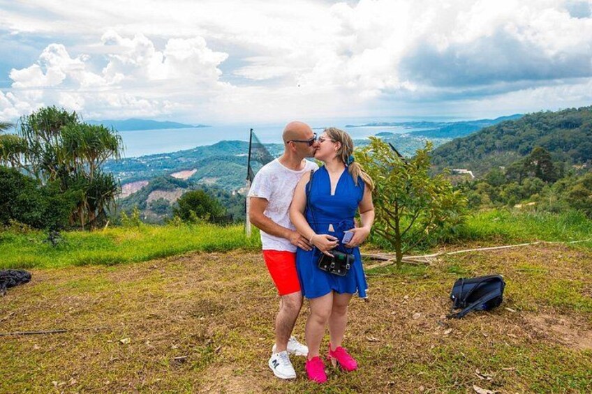 A couple embracing on a grassy hill with a scenic view of a valley and mountains in the background. 3