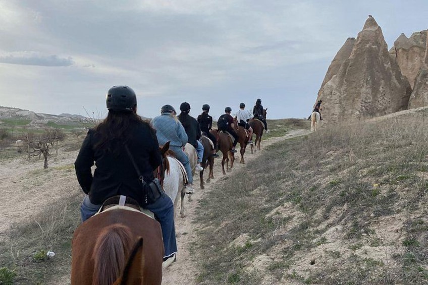 A group of people horseback riding on a dirt trail with a large rock formation in the background. 1