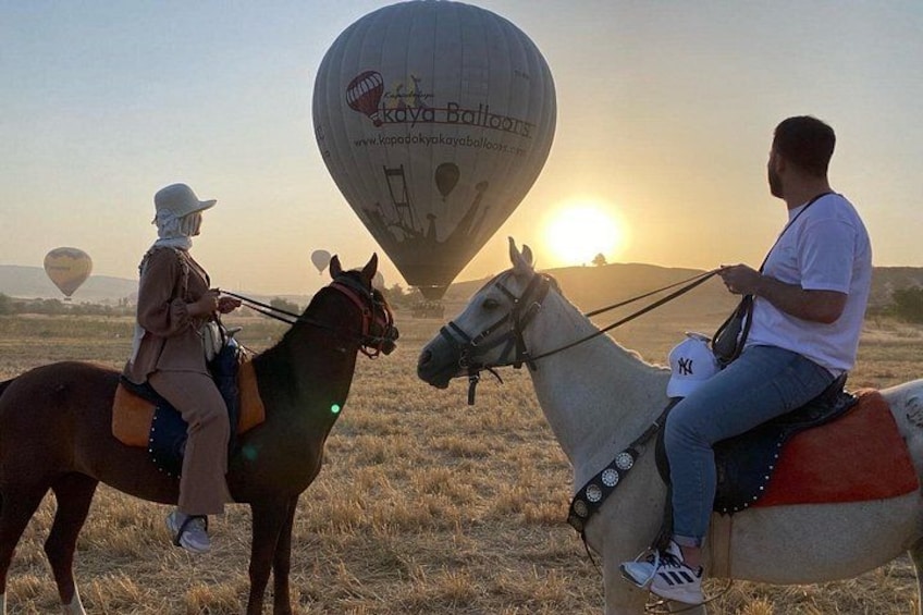 Two people riding horses with a hot air balloon in the background. 5