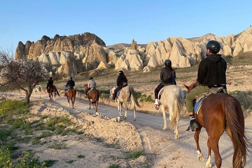 A group of people horseback riding on a dirt trail with unique rock formations in the background. 3