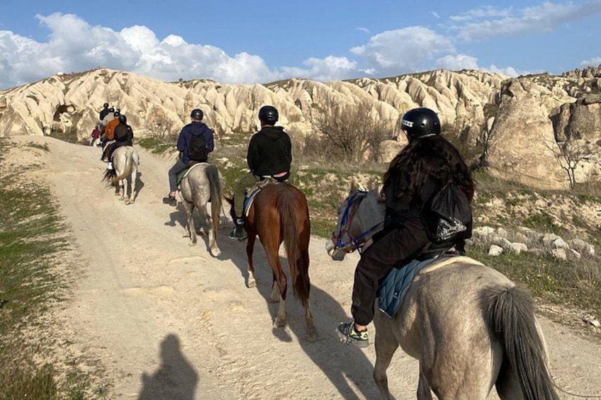 A group of people riding horses on a dirt path through a rocky landscape. 4