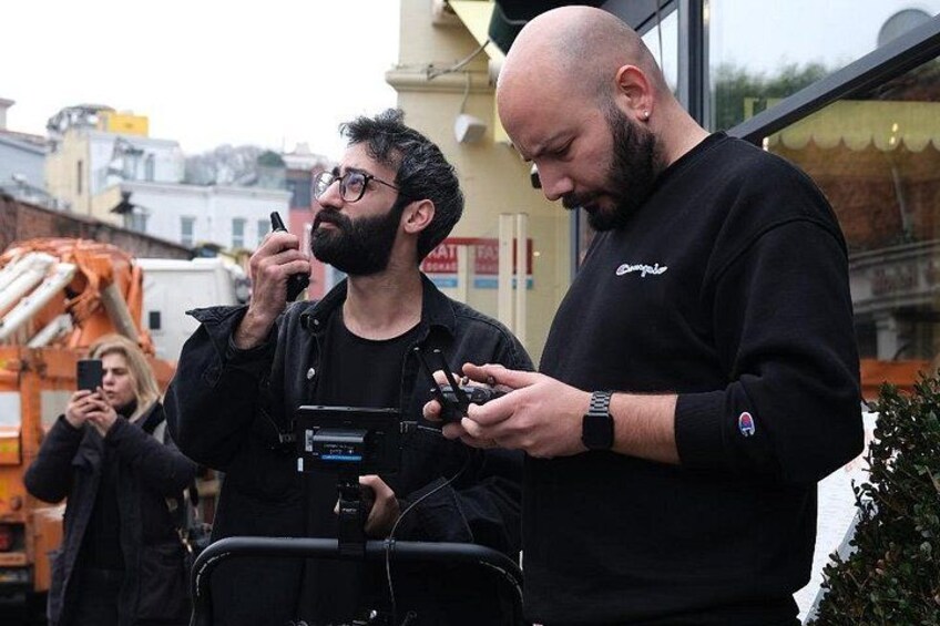 Due uomini con macchine fotografiche, uno con uno smartphone, in piedi di fronte a un cantiere edile con una gru sullo sfondo. 4