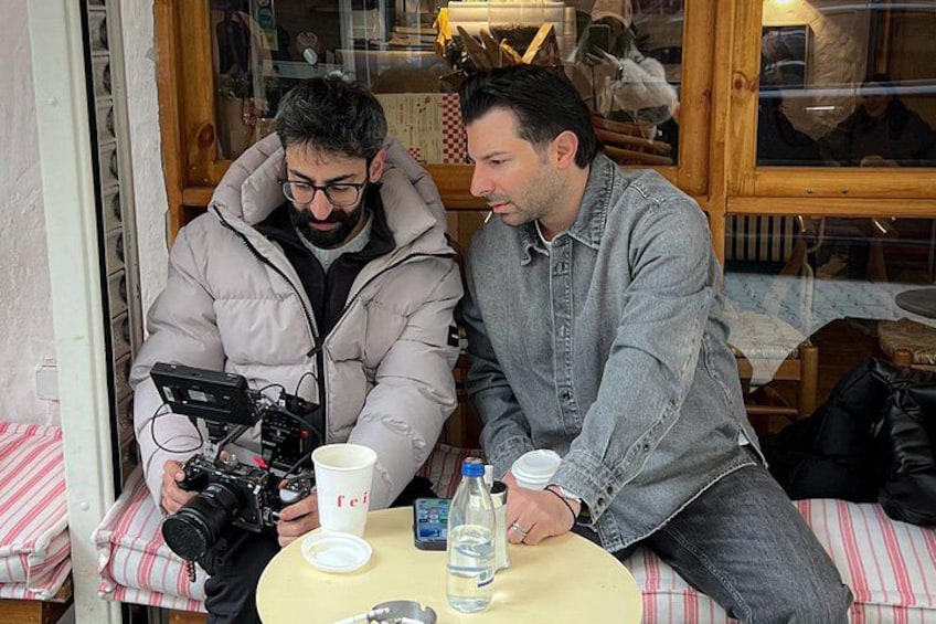 Due uomini seduti a un tavolo con una macchina fotografica e una tazza. 3