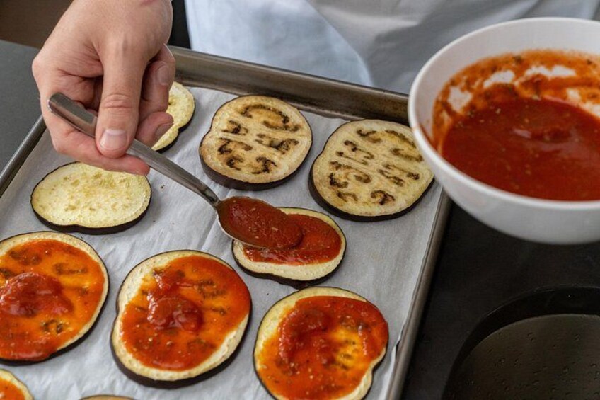 A person spreading sauce on eggplant slices on a baking tray. 2