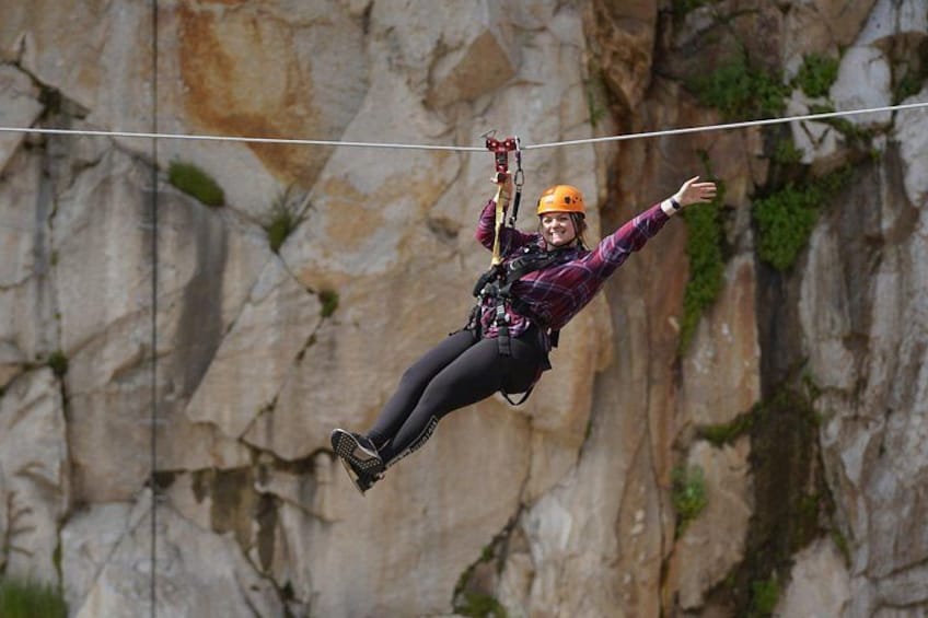 A person zip-lining with safety gear, suspended between two points, against a rocky cliff backdrop. 2