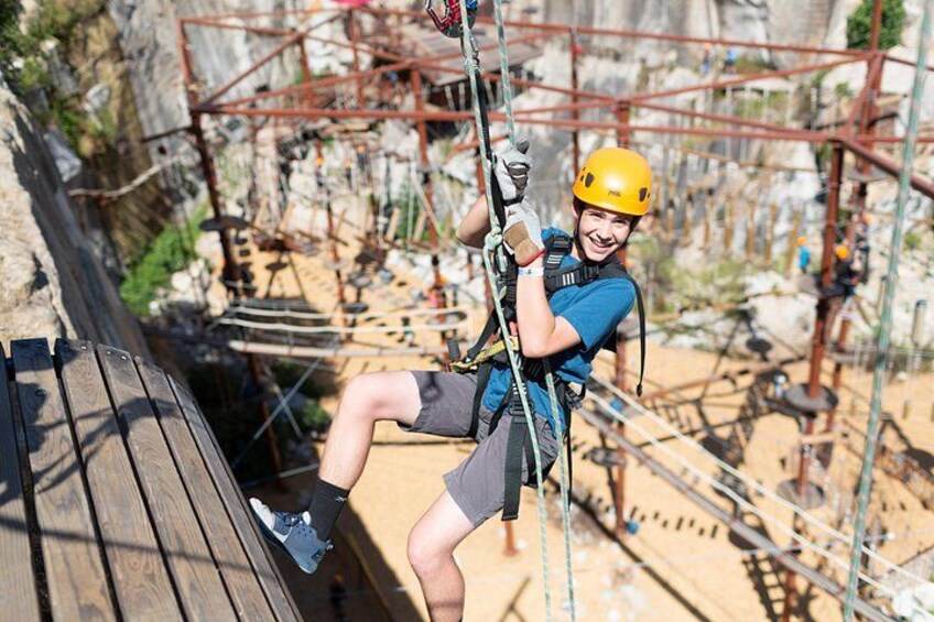 A person on a zip line with safety harness and helmet, wooden platform, and metal structures in the background. 4