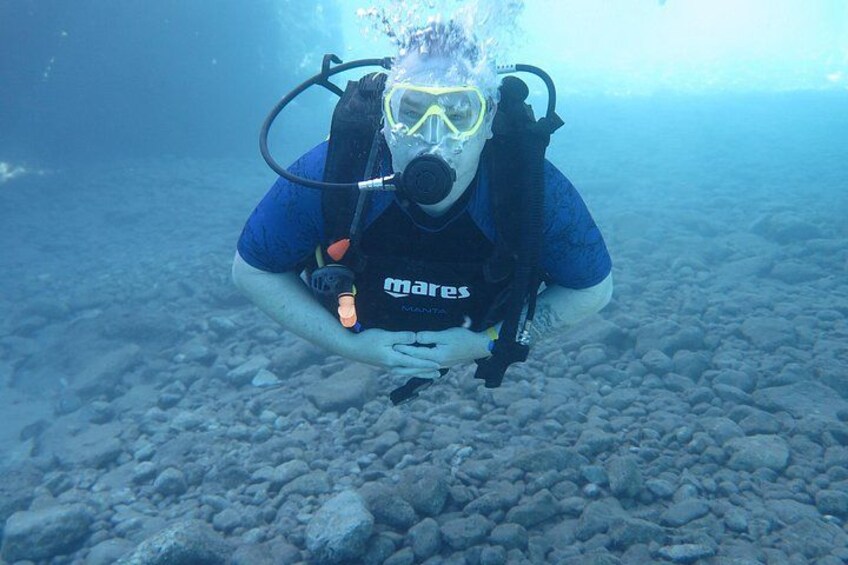 A diver underwater with a wetsuit and scuba gear, surrounded by a rocky seabed. 5