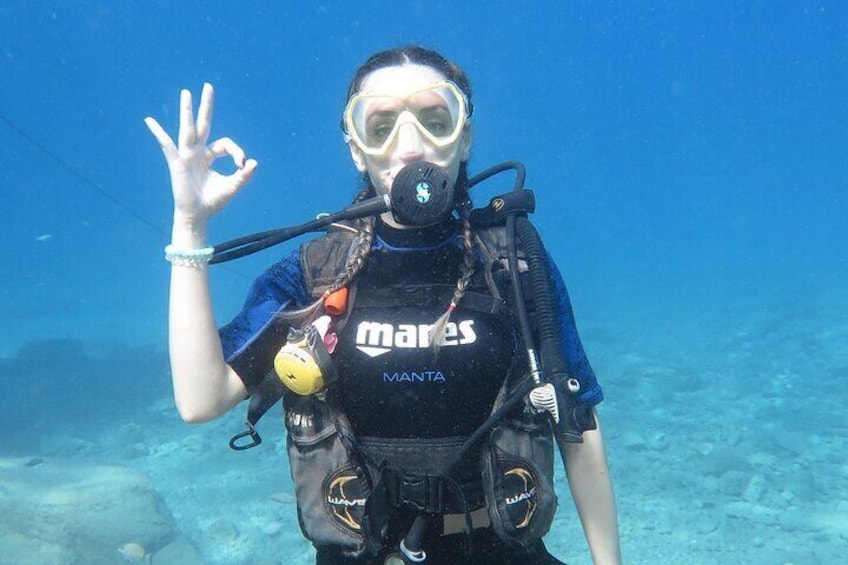 A diver underwater wearing a black wetsuit and a diving mask, with a 'MANTA' brand tank and a yellow buoyancy control device. 1