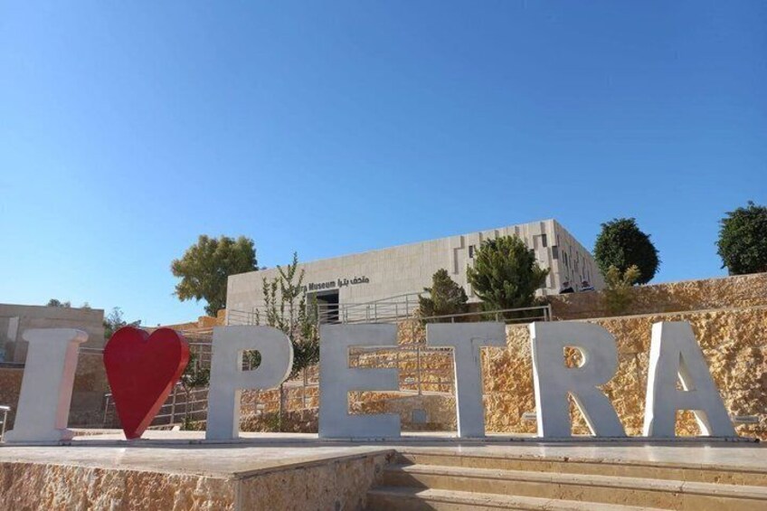 A sign with 'I ♥ PETRA' and a building in the background. 3