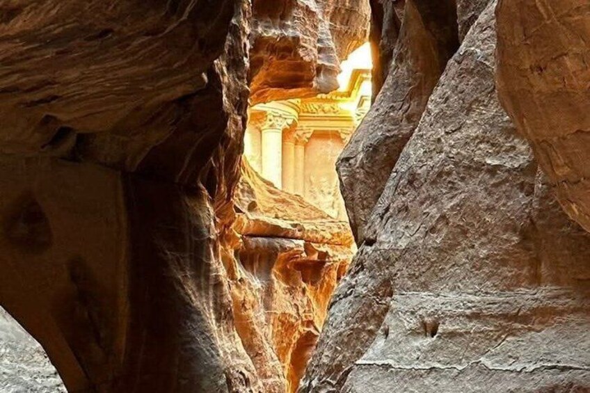 A narrow passage between rock formations with a glimpse of ancient architecture in the background. 5
