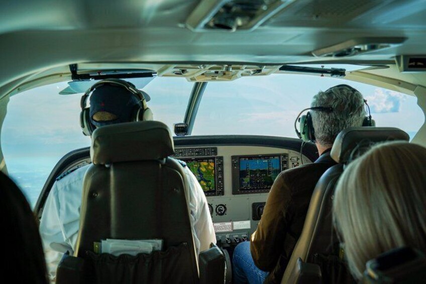 The cockpit of an aircraft with two pilots wearing headsets, a flight instrument panel, and a view of the sky through the windshield. 4