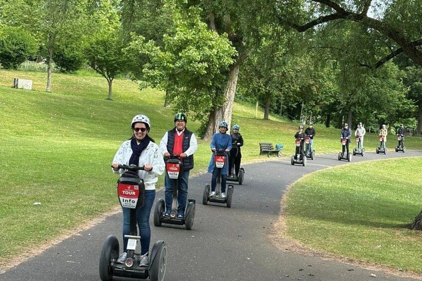 People riding Segways on a paved path in a park with trees and grass. 5