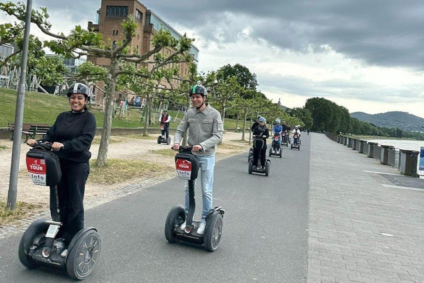 People riding segways on a paved path with trees and a building in the background. 3