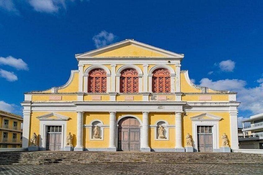 A yellow building with red window shutters, statues, and a cobblestone street. 5
