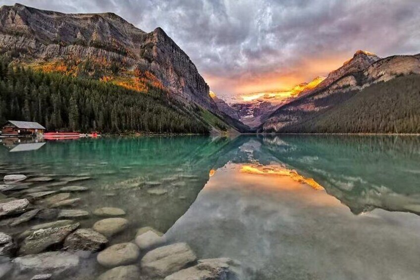A mountain lake with clear reflections, a cabin, and a forested mountain range. 1