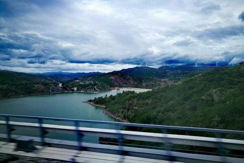 A river winding through a valley with hills, a bridge, and wind turbines in the distance. 3