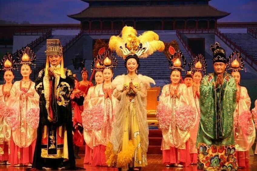A group of people in traditional costumes on a stage with a building in the background. 5