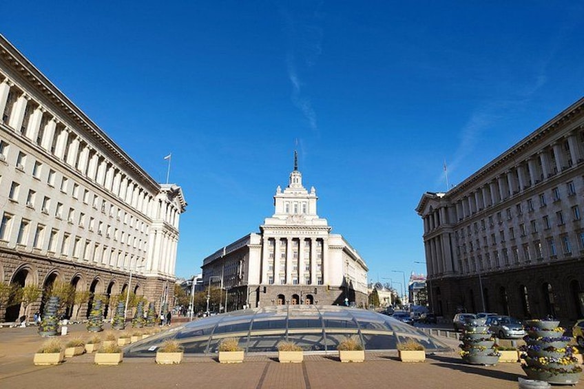 A grand building with a central tower, surrounded by symmetrical architecture and a clear blue sky. 2