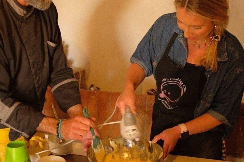 Two people preparing food, one wearing a denim shirt and apron, and the other in a dark jacket. 2