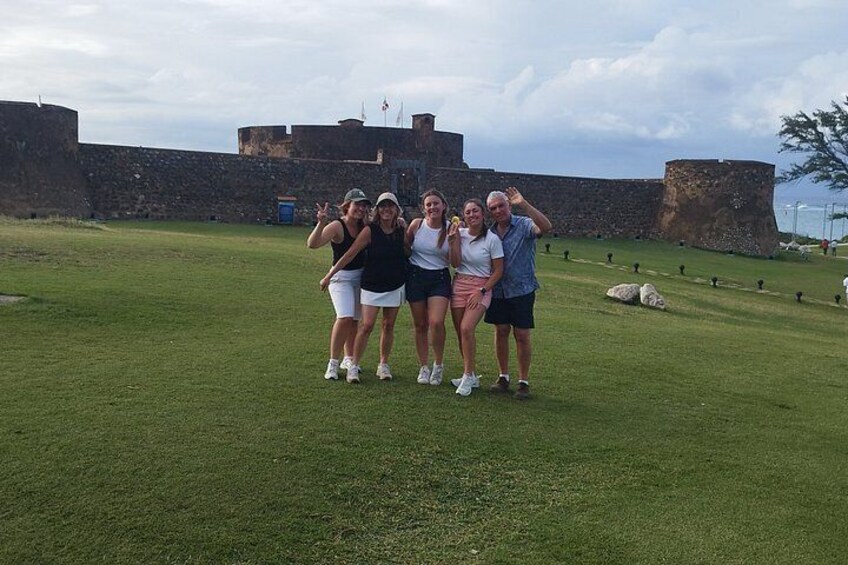 Un grupo de personas de pie en un campo cubierto de césped, con una fortaleza histórica al fondo. 4