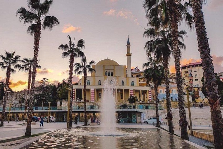 A fountain, palm trees, and a mosque with a minaret. 1