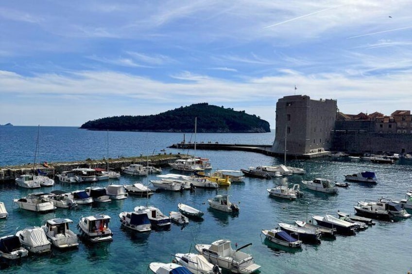 A harbor with numerous boats docked, a castle-like structure, and a small island in the background. 2