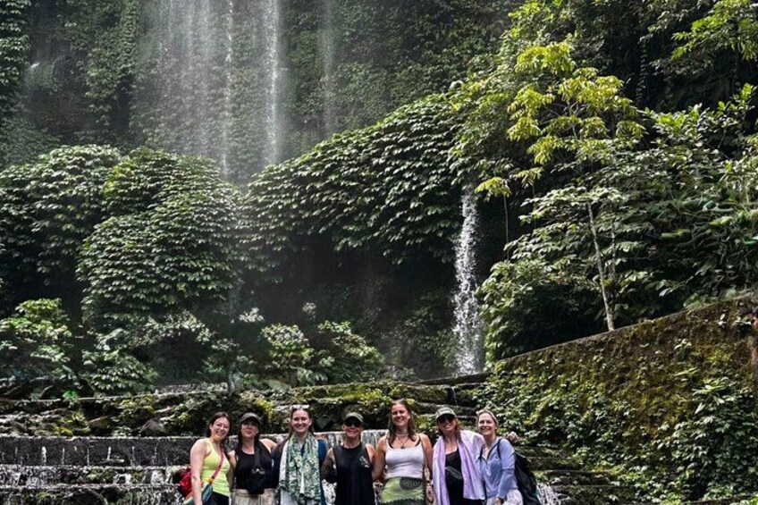 A group of people standing in a lush, green forest with a waterfall in the background. 5