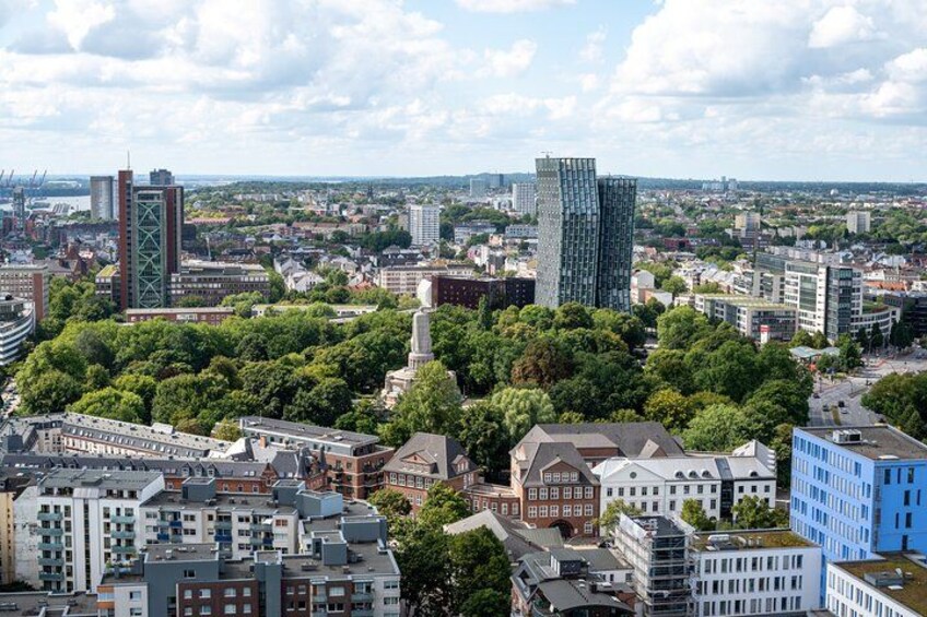 A cityscape with modern and historic buildings, a prominent tower, and a dense tree area. 3