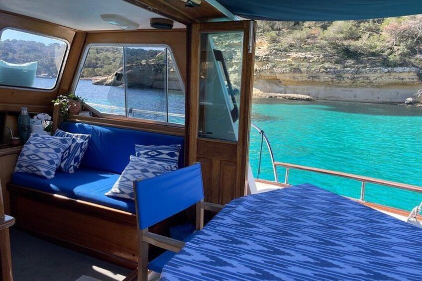 L'intérieur d'un bateau, avec un canapé bleu et un lit, une fenêtre donnant sur une eau turquoise et une côte rocheuse. 3