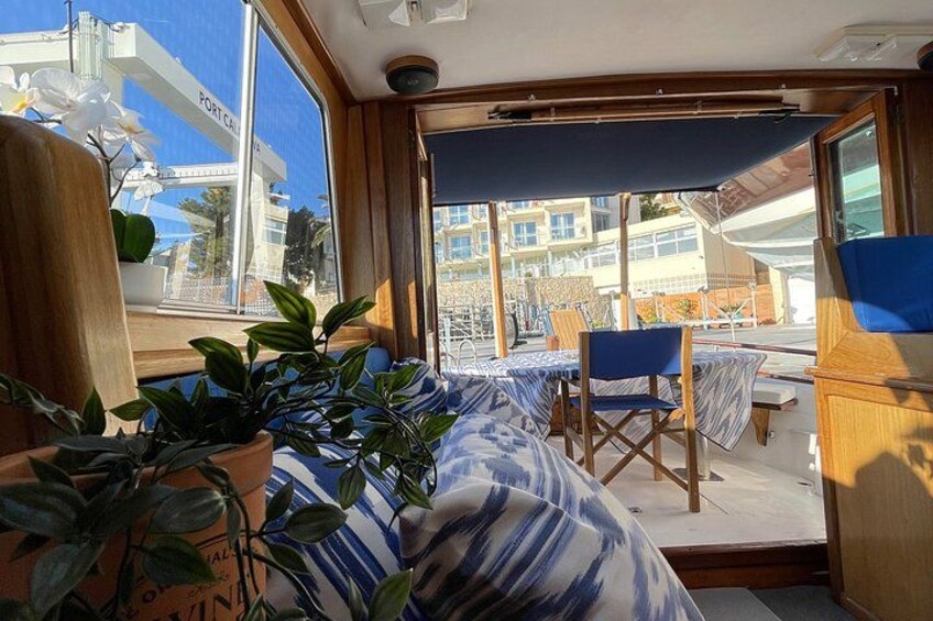 Un intérieur lumineux, baigné de soleil, avec vue sur un balcon, des plantes en pot et une table recouverte d’une nappe bleue. 4