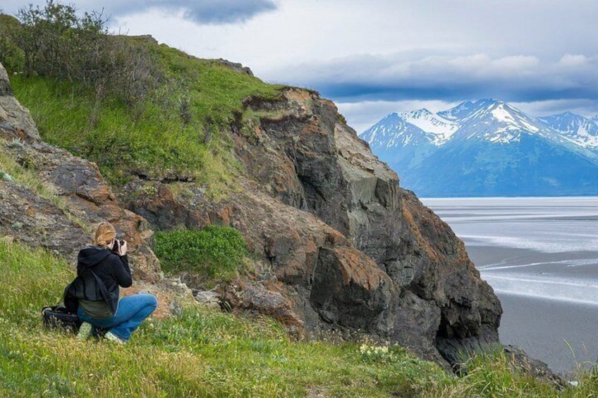 Eine Person fotografiert eine Küstenlandschaft mit Bergen im Hintergrund. 3