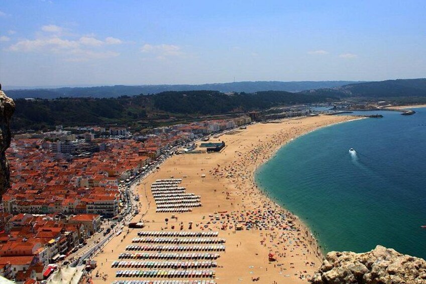 A coastal cityscape with a beach, a rocky outcrop, and a clear blue sea. 1