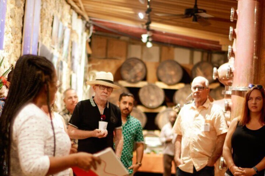A group of people in a rustic cellar with wooden barrels and a large copper still. 5