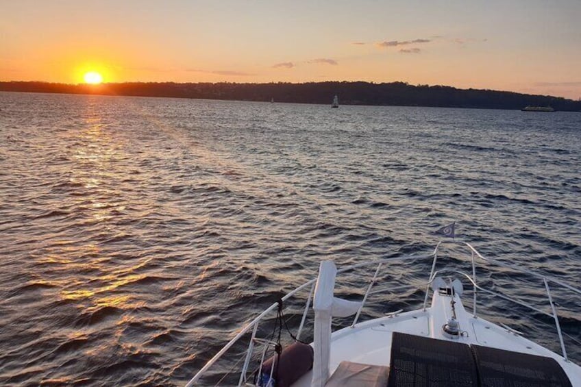A boat on calm water during sunset with a distant shoreline and a ship in the background. 4