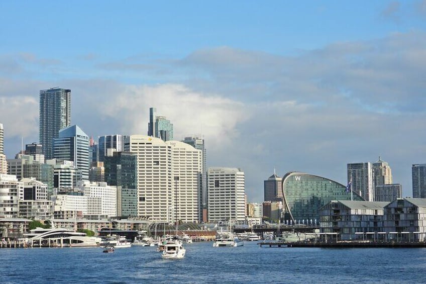A city skyline with modern buildings, a curved glass structure, and a body of water with boats. 3