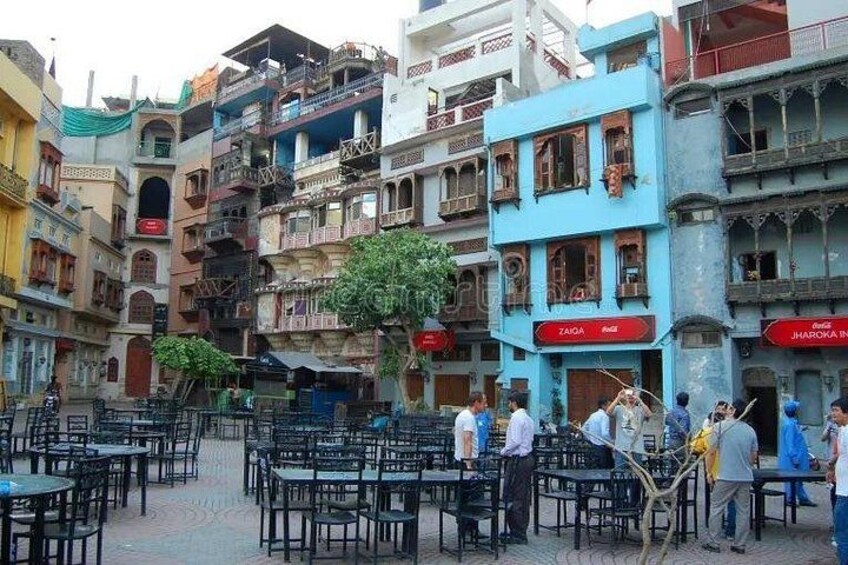 A crowded outdoor cafe with tables and chairs, surrounded by multi-story buildings with balconies and signage. 4